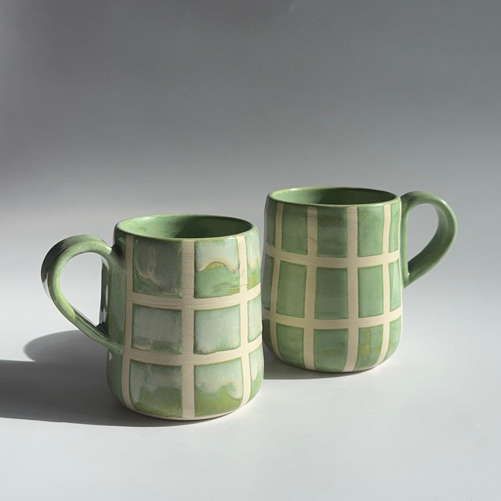 Two green ceramic mugs with grid patterns on a gray background