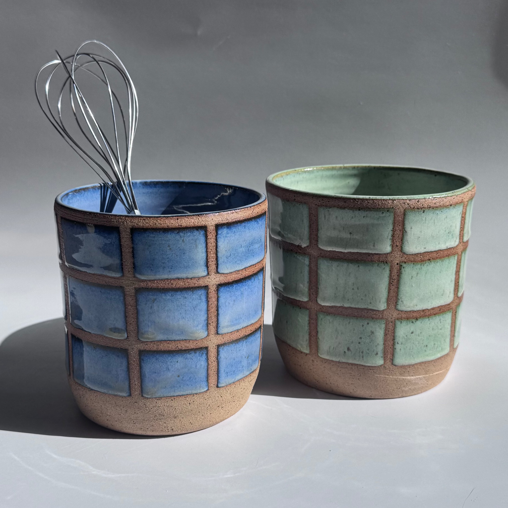 Two ceramic utensil holders with geometric patterns and a whisk on a plain background