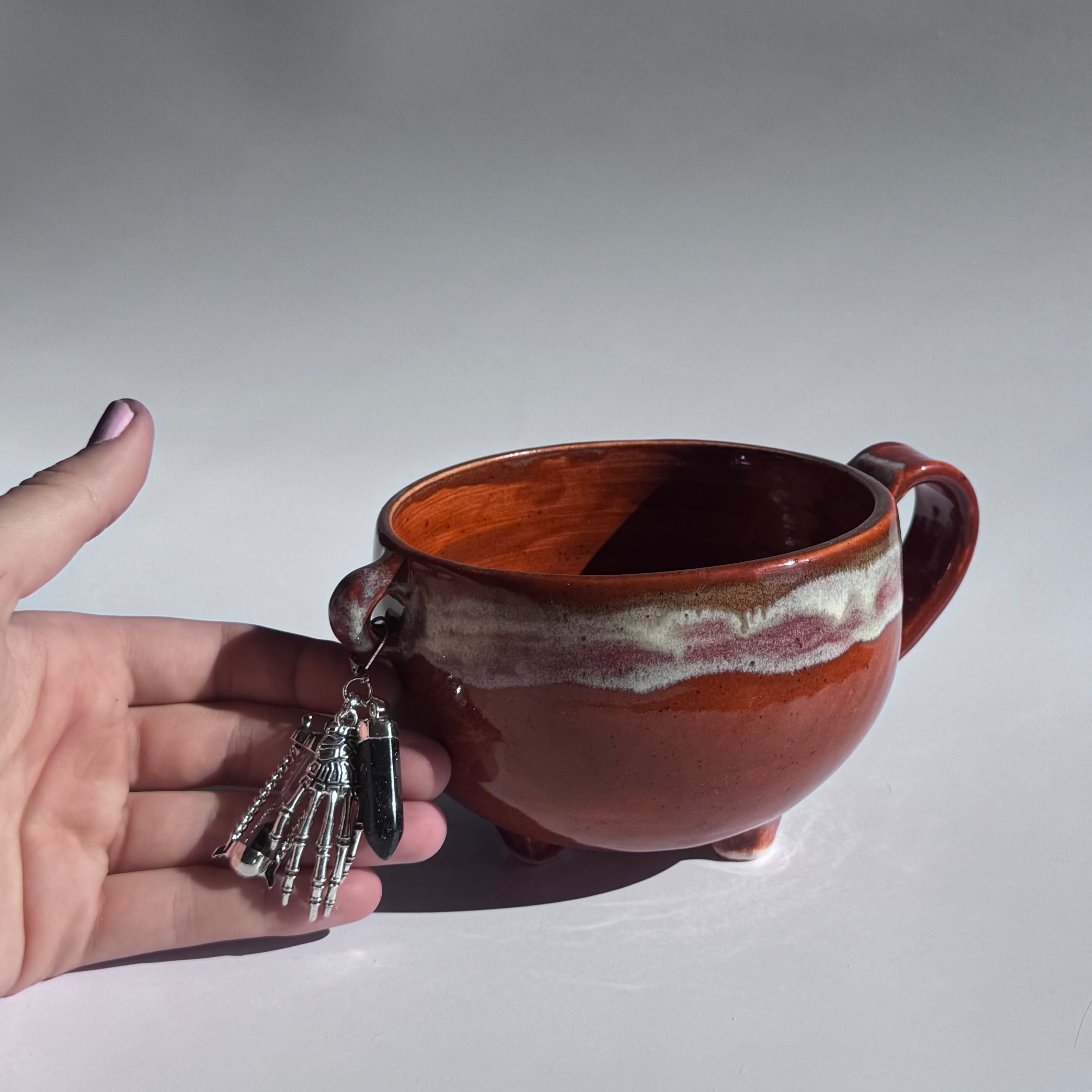 Hand holding a ceramic mug with a decorative pendant against a plain background