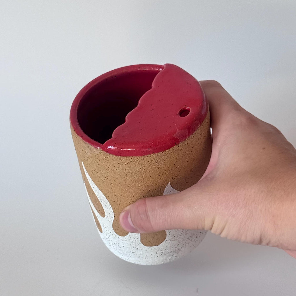 Ceramic cup with red interior held by a hand on a white background