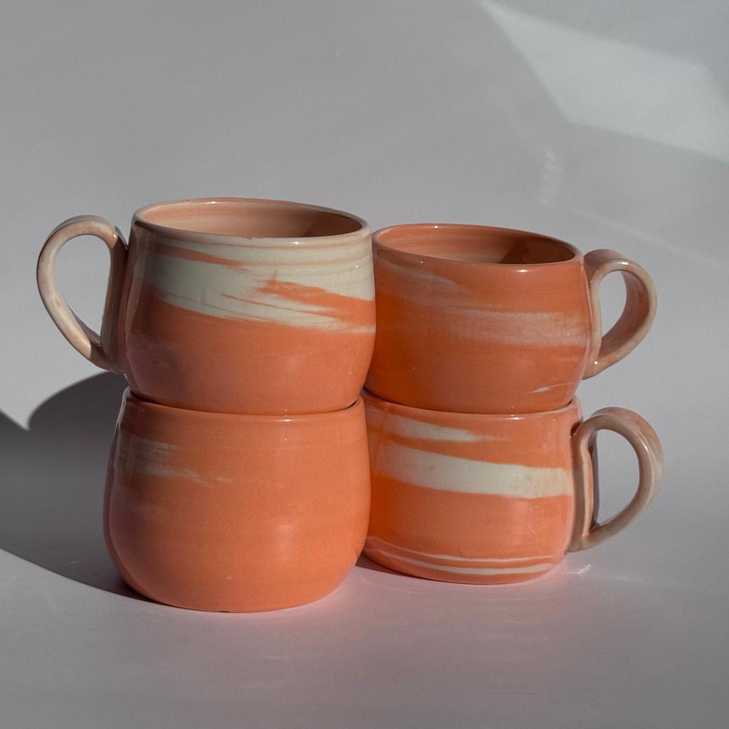 Set of four ceramic mugs with orange and white stripes on a white background