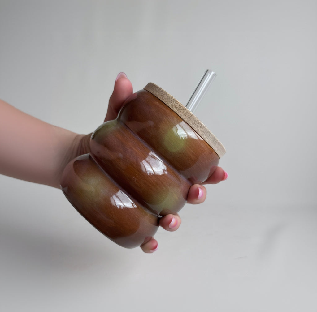 Hand holding a brown ceramic tumbler with a straw on a plain background