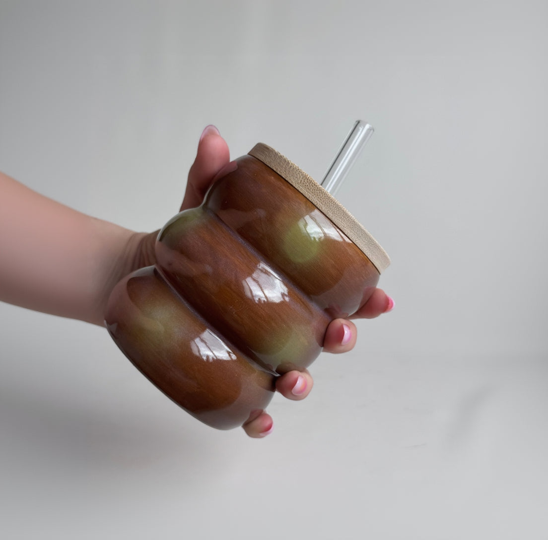 Hand holding a brown ceramic tumbler with a straw on a plain background