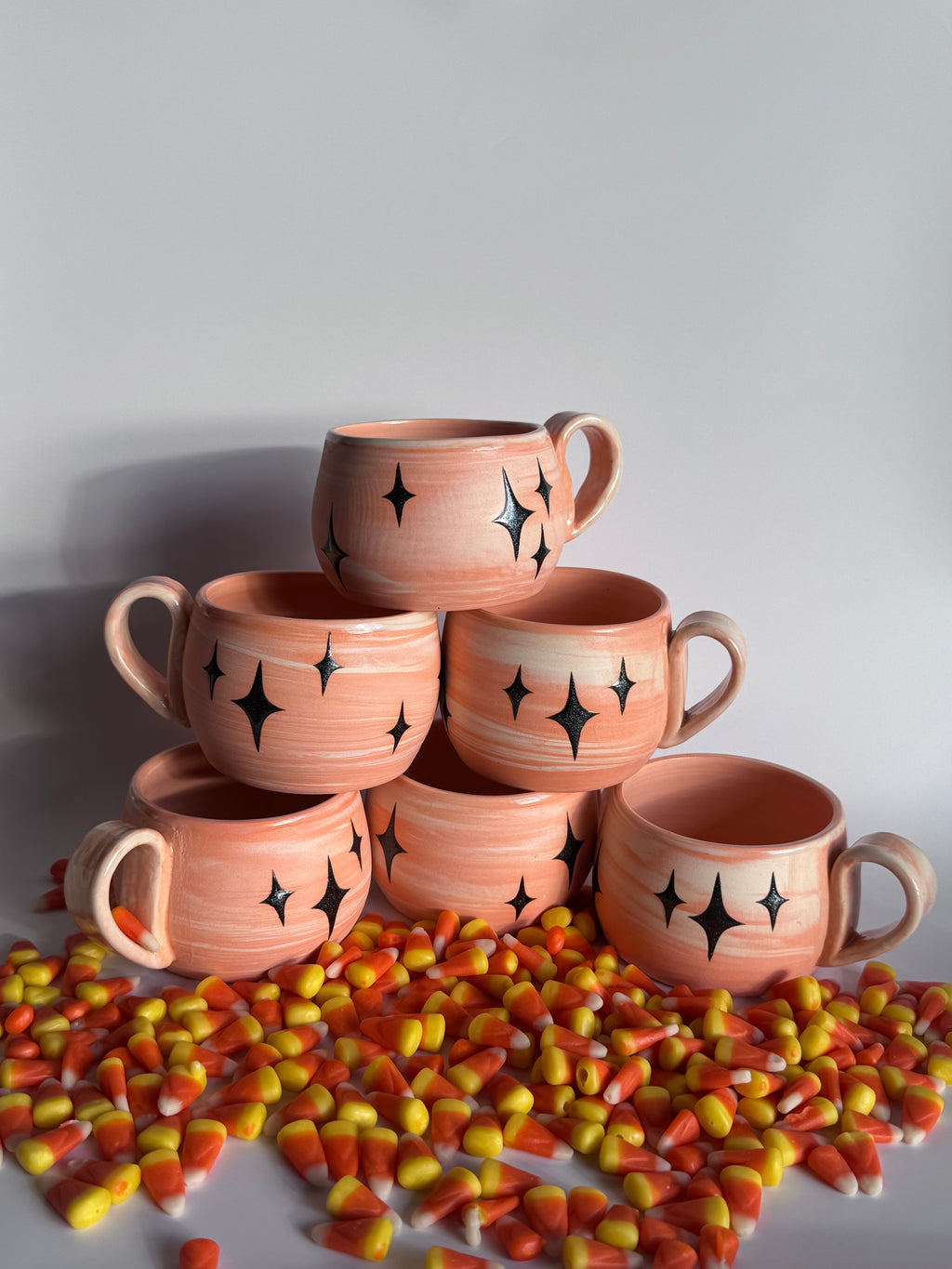 Pumpkin-shaped mugs with black star designs on a white background with candy corn.