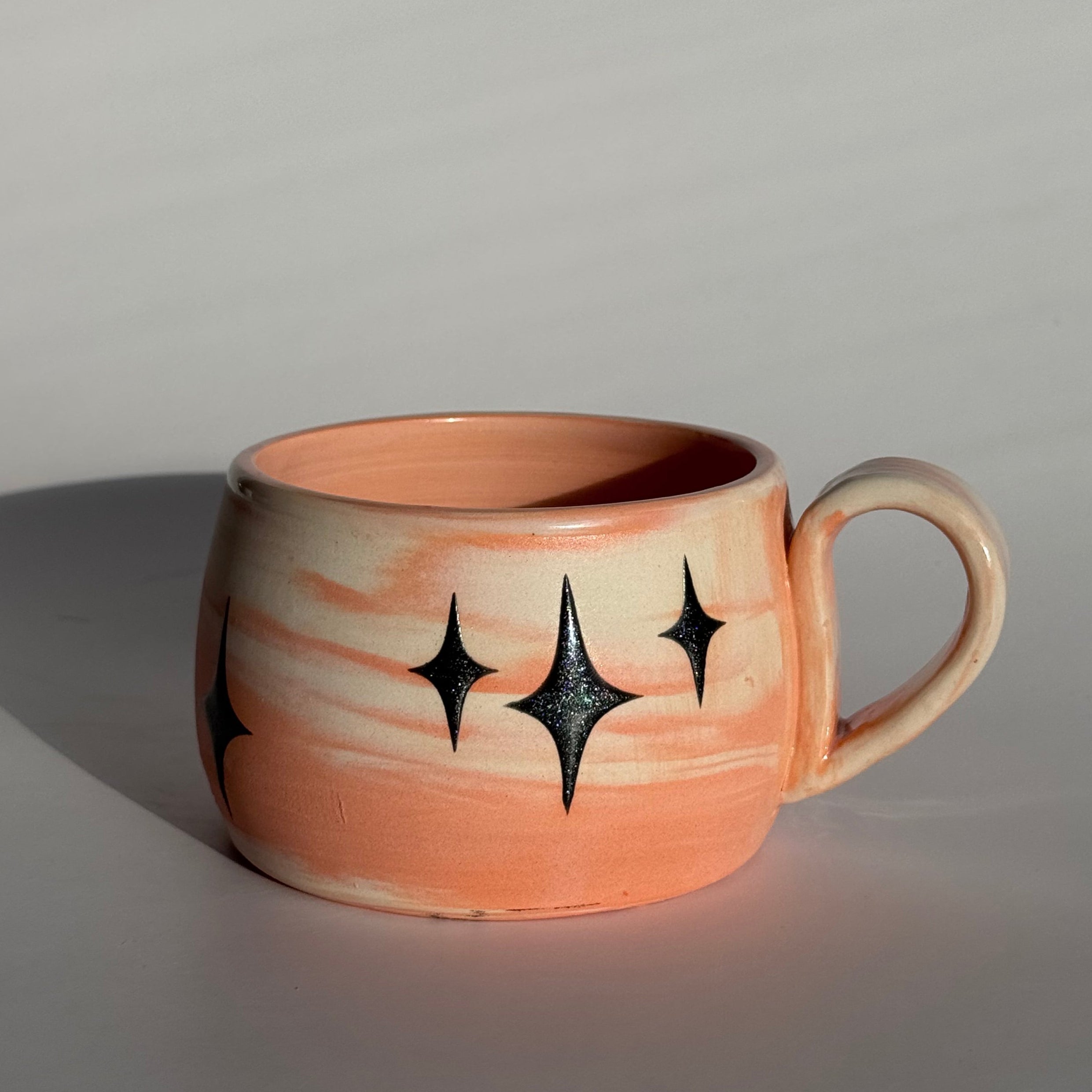 Ceramic mug with star patterns and orange and white swirled clay. 