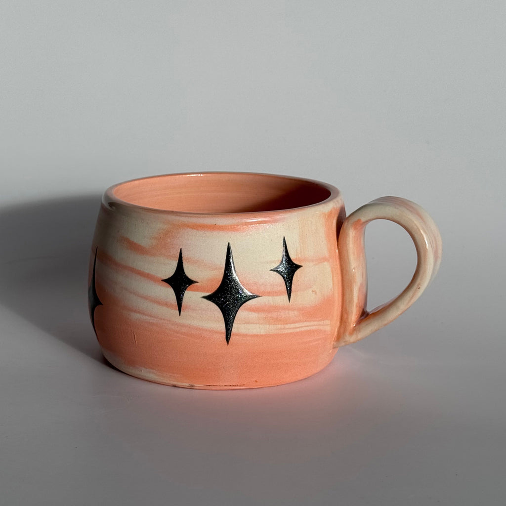 Ceramic mug with star patterns and orange and white swirled clay. 