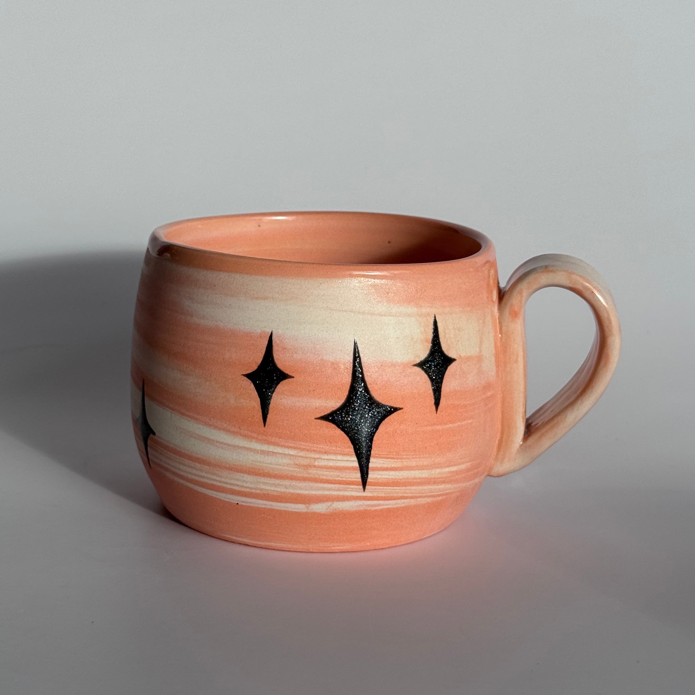 Ceramic mug with star patterns and orange and white swirled clay. 