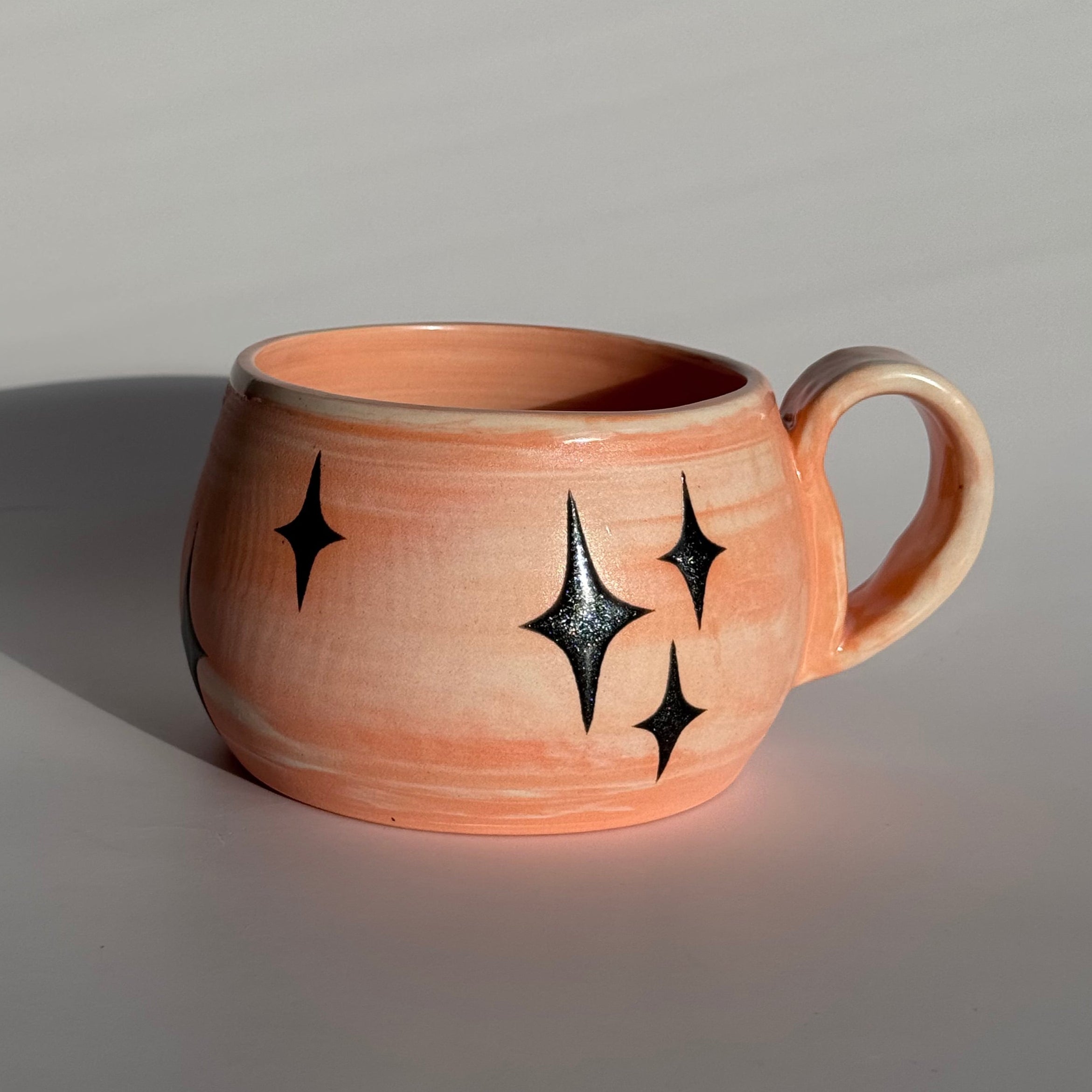 Ceramic mug with star patterns and orange and white swirled clay. 