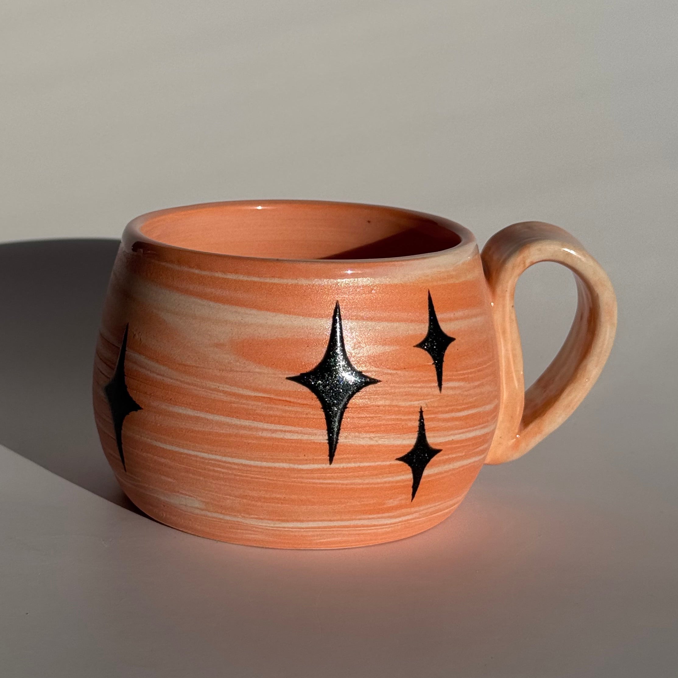 Ceramic mug with star patterns and orange and white swirled clay. 