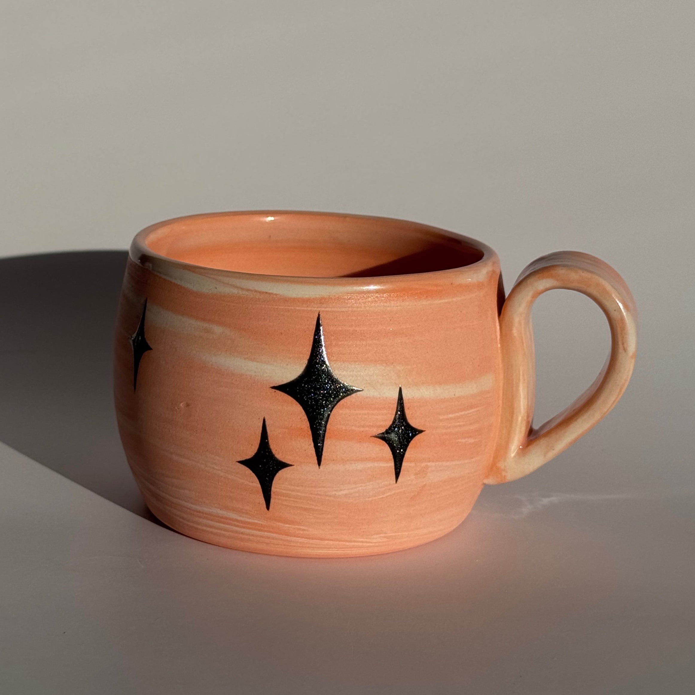 Ceramic mug with star patterns and orange and white swirled clay. 