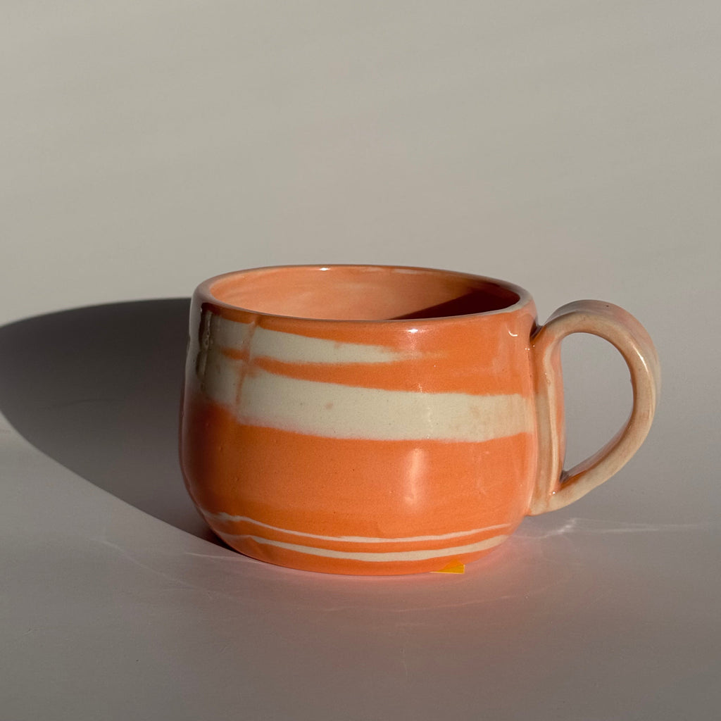 Orange and white striped mug hanging on a white wall