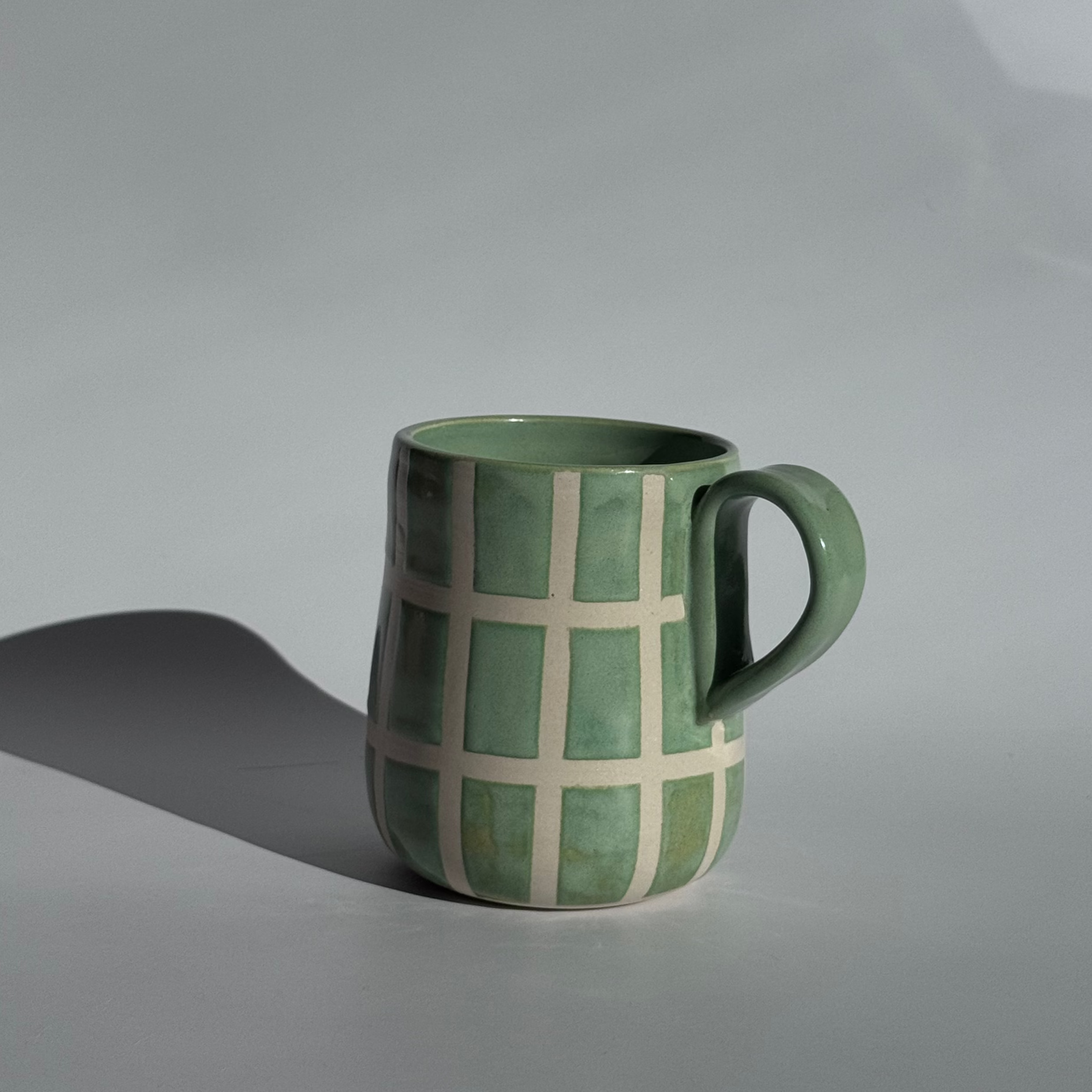 Green ceramic mug with a checkered pattern on a gray background