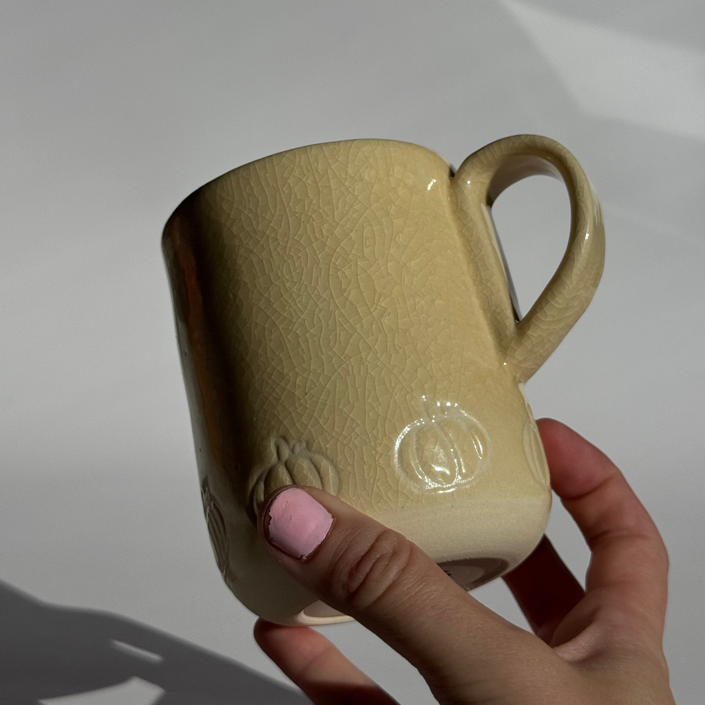 Beige mug with a subtle pattern held by a hand against a white background