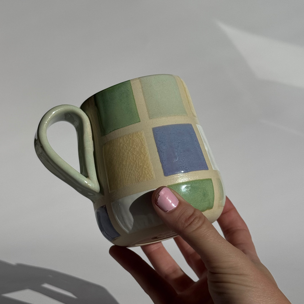 Hand holding a mug with a checkered pattern on a plain background