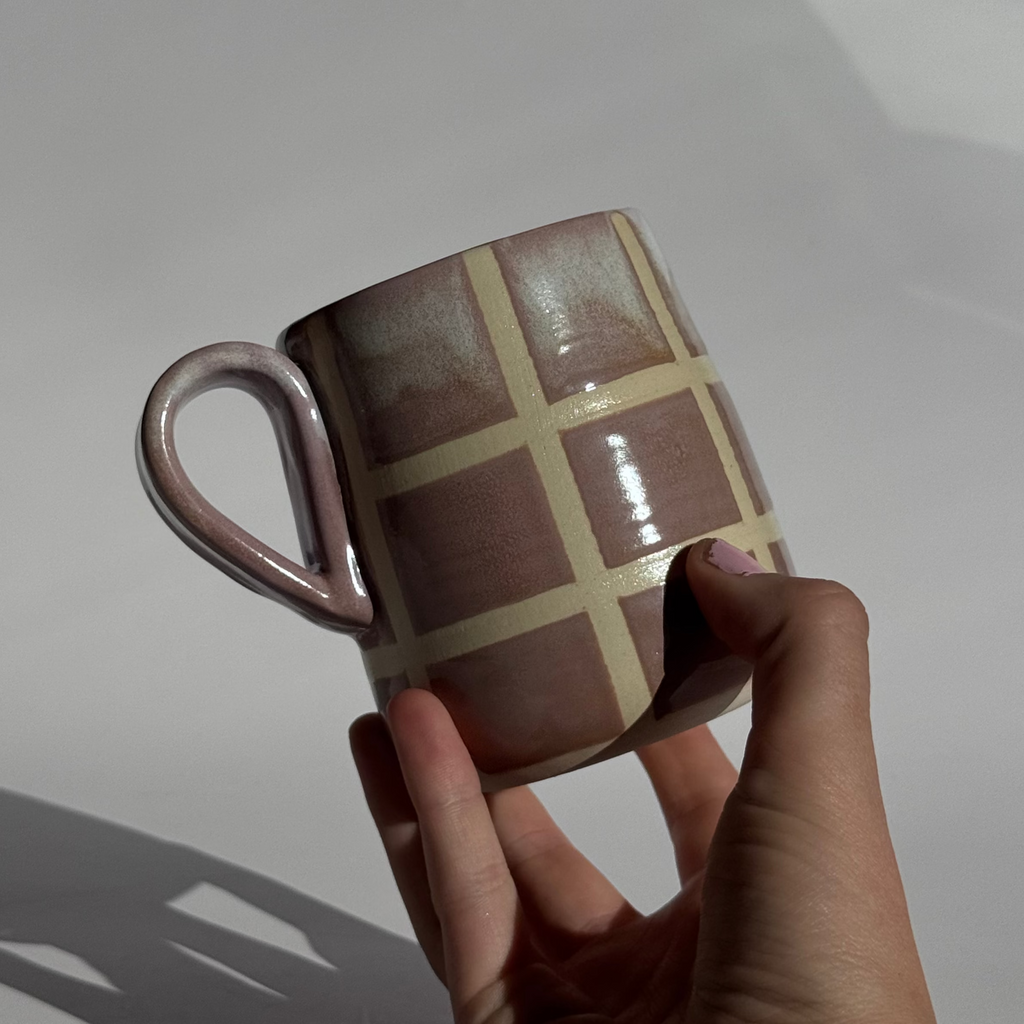 Hand holding a ceramic mug with a grid pattern against a plain background