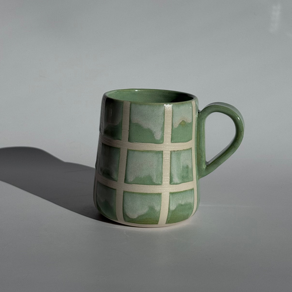 Green mug with a grid pattern held by a hand on a light gray background