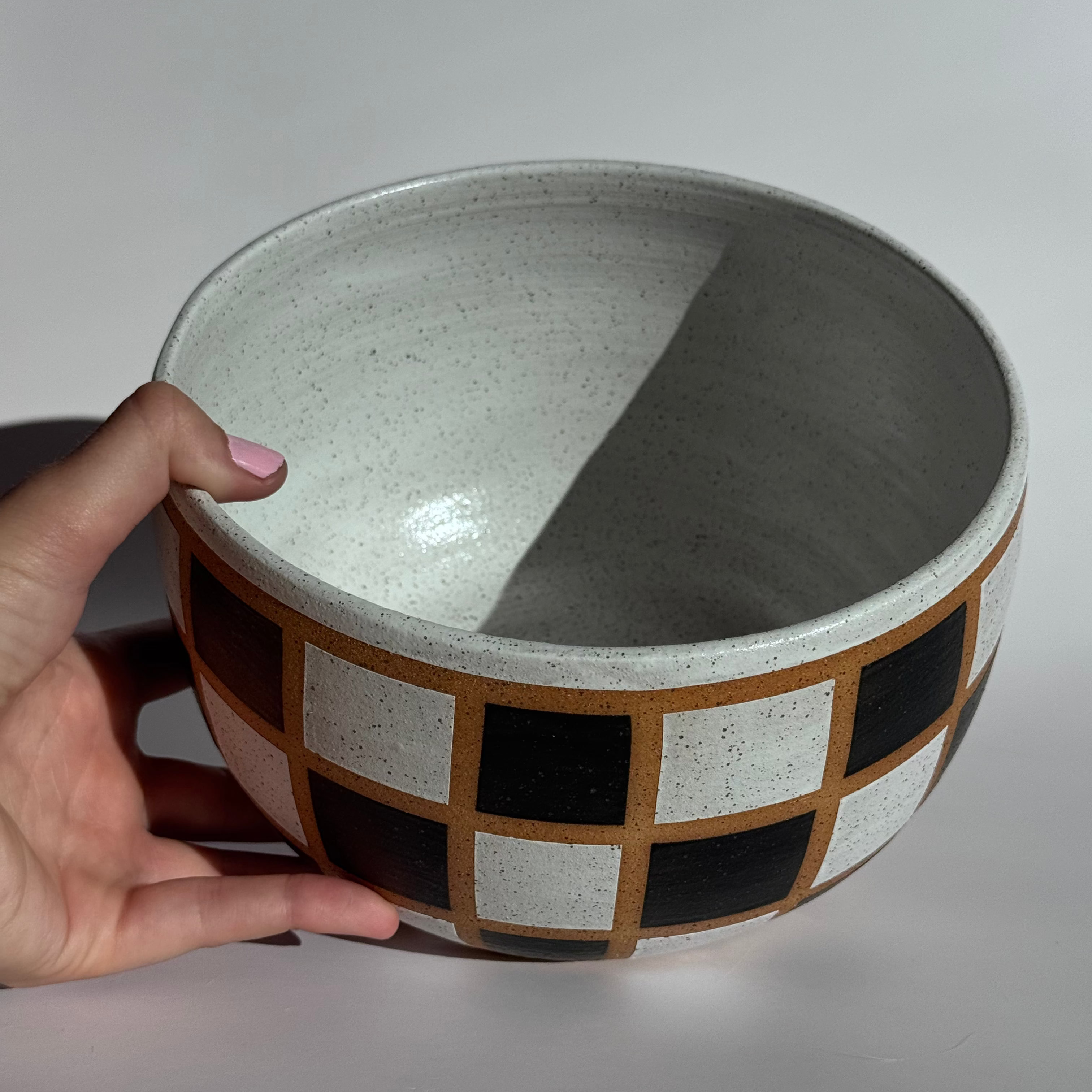 Ceramic bowl with geometric pattern held by a hand on a light gray background